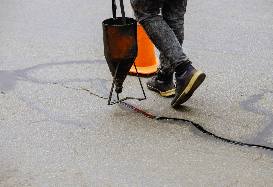 Worker sealing a crack in an asphalt surface with hot crack sealant.